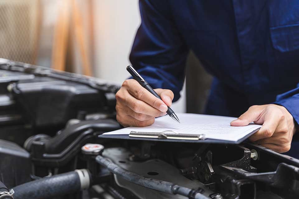 Auto check up and car service shop concept. Mechanic writing job checklist to clipboard to estimate repair quotation to client at workshop garage.